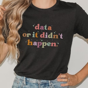 May include: Black t-shirt with the text "data or it didn't happen" in colorful, retro-style lettering. The shirt has a crew neck and short sleeves. The design includes stars around the text.
