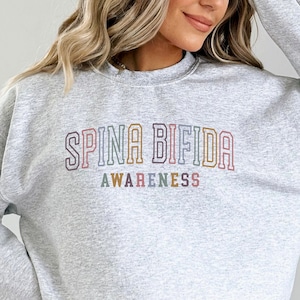 May include: Gray sweatshirt with the text "Spina Bifida Awareness" in rainbow colors.