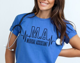 Puede incluir: Una camiseta azul con un gráfico de latido del corazón negro y el texto "MLA - Medical Assistant". Un estetoscopio está drapeado alrededor del cuello de la camiseta.