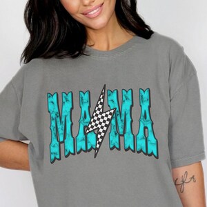 Puede incluir: Una camiseta gris con un gr&aacute;fico azul turquesa que dice "MAMA" con un rayo a cuadros en el medio.
