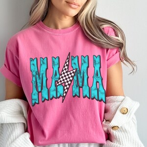 Puede incluir: Camiseta rosa de manga corta con un gr&aacute;fico azul turquesa que dice "MAMA" con un rayo a cuadros en el centro.