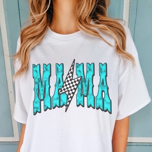 Puede incluir: Camiseta blanca de gran tama&ntilde;o con un gr&aacute;fico azul turquesa que dice "MAMA" con un rayo a cuadros en el medio.