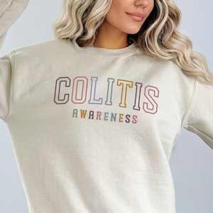 May include: A light beige sweatshirt with the text "COLITIS AWARENESS" in rainbow colored letters.