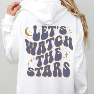 May include: White hooded sweatshirt with a blue and gold graphic that says "Let's Watch The Stars" with a crescent moon and stars.