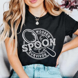 May include: A black t-shirt with a white graphic design of a wooden spoon with the text "Wooden Spoon Survivor".