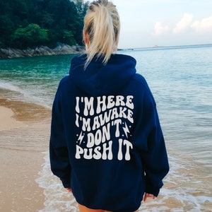 May include: A navy blue hooded sweatshirt with the text "I'M HERE I'M AWAKE DON'T PUSH IT" printed in white on the back.