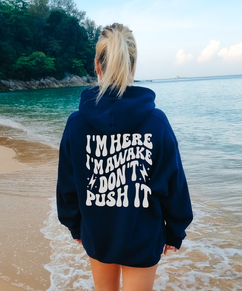 May include: A navy blue hooded sweatshirt with the text "I'M HERE I'M AWAKE DON'T PUSH IT" printed in white on the back.