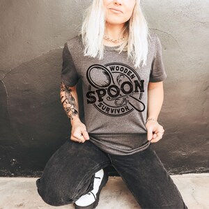May include: A gray t-shirt with a black graphic of a wooden spoon and the text "Wooden Spoon Survivor".