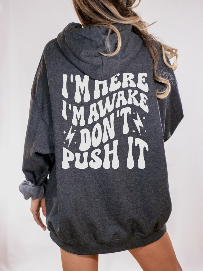 May include: A dark gray hooded sweatshirt with the text "I'm here I'm awake Don't push it" in white, stylized lettering.