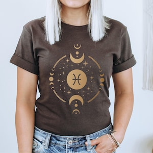 May include: A dark brown t-shirt with a gold graphic of the Pisces zodiac sign surrounded by moons and stars.