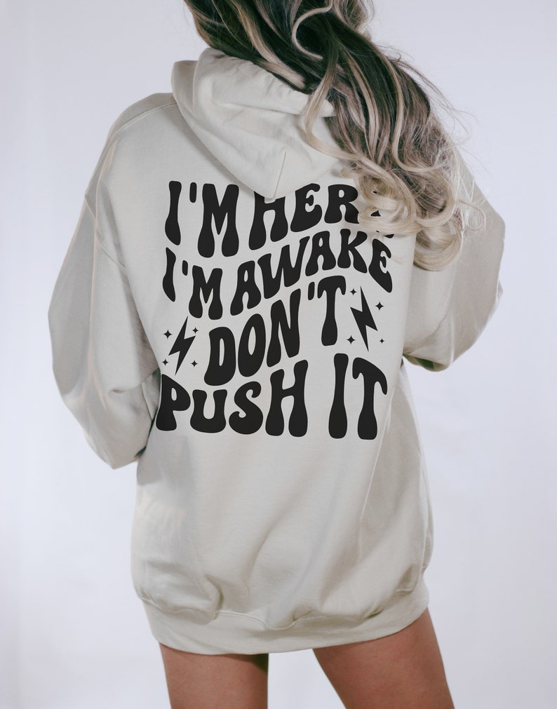 May include: A light beige hoodie with a black graphic print that reads "I'm here I'm awake Don't push it" in a retro font.
