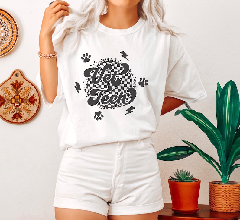 Puede incluir: Camiseta blanca con un dise&ntilde;o circular de cuadros blancos y negros que dice "Vet Tech" en una fuente retro. El dise&ntilde;o tambi&eacute;n incluye huellas de patas y rayos.