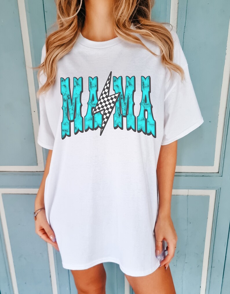 Puede incluir: Camiseta blanca de gran tama&ntilde;o con un gr&aacute;fico azul turquesa que dice "MAMA" con un rayo a cuadros en el medio.