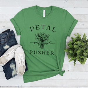 May include: Green t-shirt with a black graphic of a bouquet of flowers and the text "PETAL professional PUSHER".