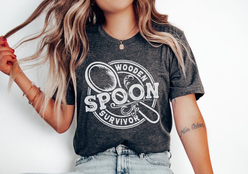 May include: A dark gray t-shirt with a white graphic of a wooden spoon in a circle with the text "Wooden Spoon Survivor".
