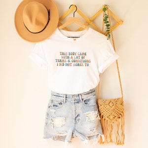 May include: White t-shirt with a colorful graphic that reads "This body came with a lot of terms & conditions I did not agree to".