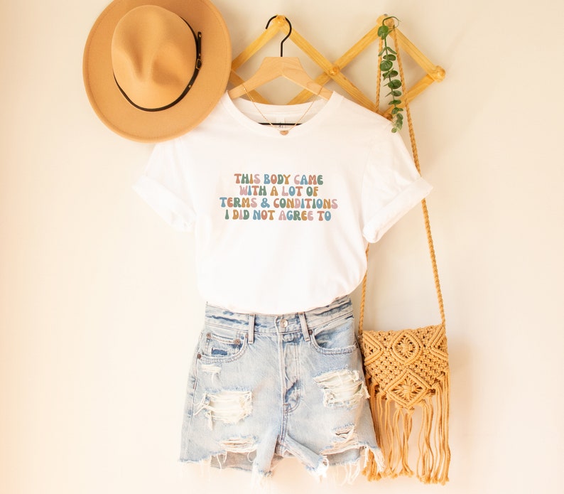 May include: White t-shirt with a colorful graphic that reads "This body came with a lot of terms & conditions I did not agree to".
