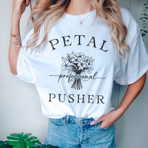 May include: White t-shirt with black text that reads "PETAL professional PUSHER" and a black floral graphic.