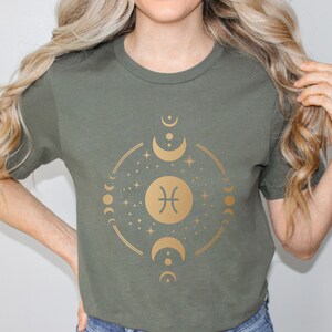 May include: A green t-shirt with a gold graphic of the Pisces zodiac sign surrounded by moons and stars.