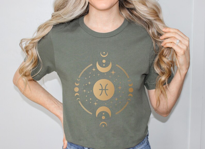 May include: A green t-shirt with a gold graphic of the Pisces zodiac sign surrounded by moons and stars.