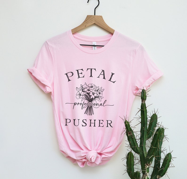 May include: Pink t-shirt with a black graphic that says "PETAL professional PUSHER" and a bouquet of flowers.