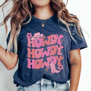 May include: A navy blue t-shirt with a pink and white graphic design that says "Howdy Howdy Howdy" with a cowboy hat and boot.