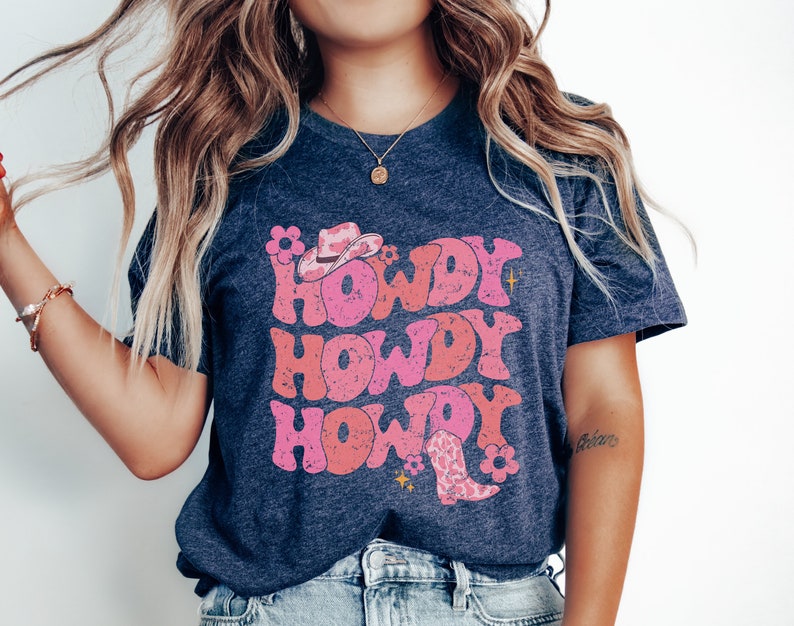May include: A navy blue t-shirt with a pink and white graphic design that says "Howdy Howdy Howdy" with a cowboy hat and boot.