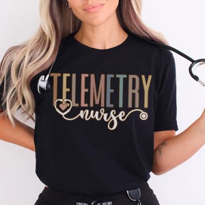 May include: A black t-shirt with the text "Telemetry Nurse" in colorful letters. A stethoscope is draped over the shirt and held by a person.