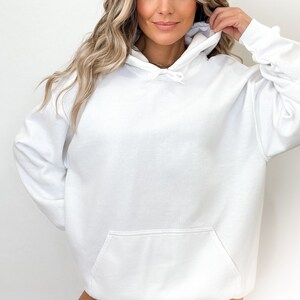May include: A white hooded sweatshirt with a front pocket and drawstring hood. The sweatshirt is made of a soft material and has long sleeves. The overall style is casual and comfortable, suitable for everyday wear.