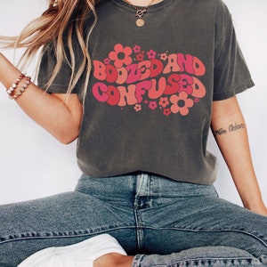 May include: A dark grey t-shirt with a retro-style graphic that says "Boozed and Confused" in pink and red letters with flowers surrounding the text.