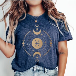 May include: A navy blue t-shirt with a gold zodiac symbol for Pisces, surrounded by a circle of moons and stars.