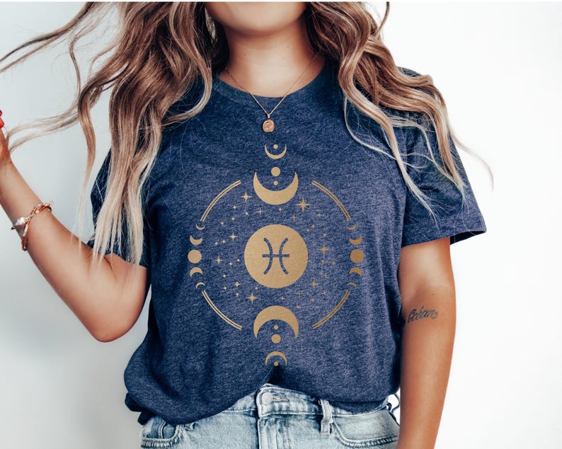 May include: A navy blue t-shirt with a gold zodiac symbol for Pisces, surrounded by a circle of moons and stars.