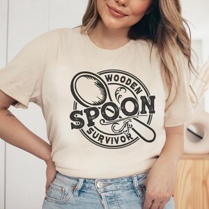 May include: A beige t-shirt with a black graphic of a wooden spoon and the text "Wooden Spoon Survivor".