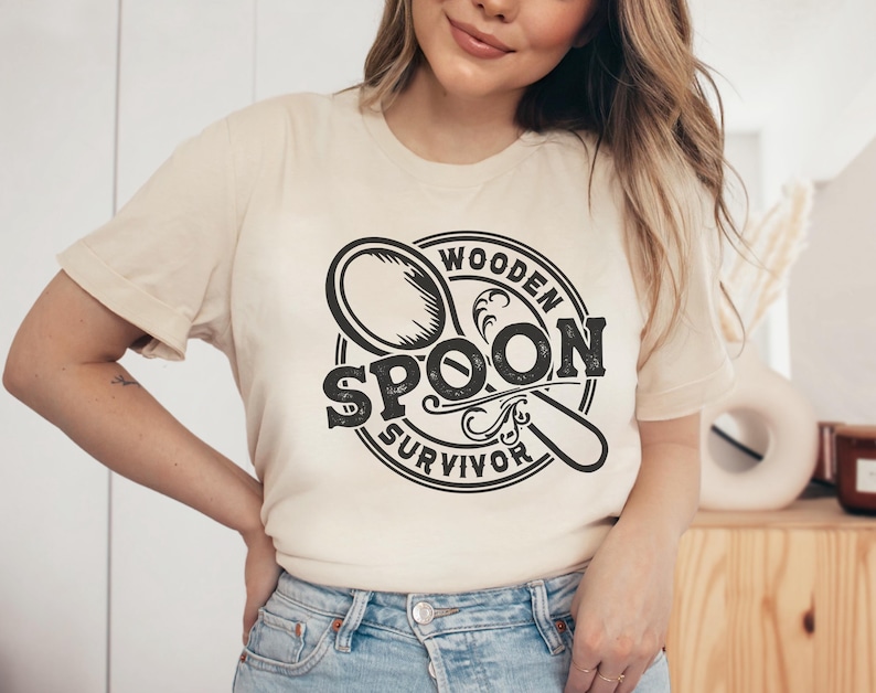 May include: A beige t-shirt with a black graphic of a wooden spoon and the text "Wooden Spoon Survivor".