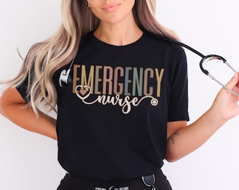 May include: Black t-shirt with the words "EMERGENCY nurse" in a multi-coloured design. A stethoscope is held in the hand. The shirt is a crew neck style.