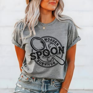May include: A gray t-shirt with a black graphic of a wooden spoon and the text "Wooden Spoon Survivor".