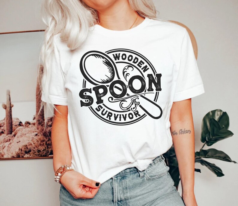 May include: White t-shirt with a black and white graphic design of a wooden spoon with the text "Wooden Spoon Survivor".