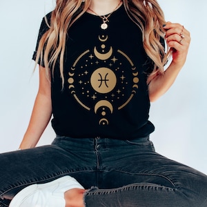 May include: Black t-shirt with a gold Pisces zodiac symbol surrounded by a circle of moons and stars.