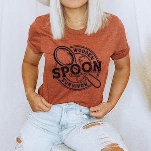 May include: A rust-colored t-shirt with a black graphic of a wooden spoon and the text "Wooden Spoon Survivor".