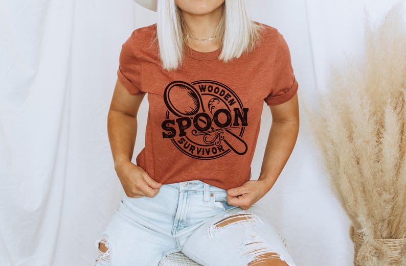 May include: A rust-colored t-shirt with a black graphic of a wooden spoon and the text "Wooden Spoon Survivor".