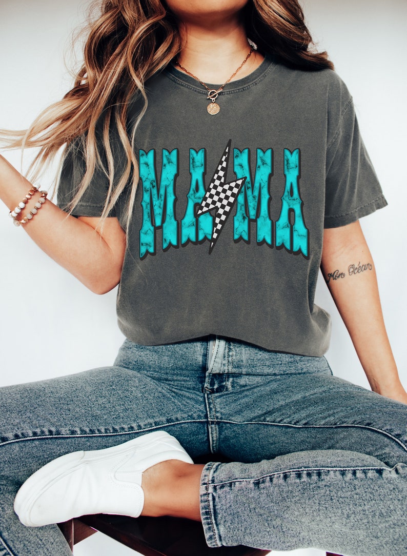 Puede incluir: Una camiseta gris con un gr&aacute;fico azul turquesa que dice "MAMA" con un rayo a cuadros en el medio.