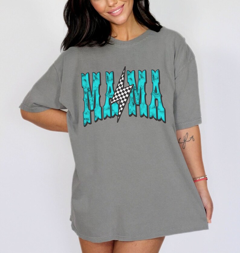 Puede incluir: Una camiseta gris con un gr&aacute;fico azul turquesa que dice "MAMA" con un rayo a cuadros en el medio.