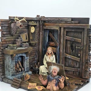 Puede incluir: Un diorama detallado del interior de una cabaña rústica con una chimenea de piedra, una cabeza de ciervo montada en la pared, un reloj de pie y dos figuras. Una figura está sentada en el suelo mientras la otra emerge de una trampilla de madera.