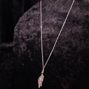 May include: A silver chain necklace with a small, silver and purple pendant. The pendant is shaped like a cluster of grapes.