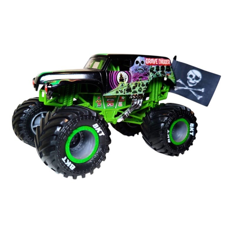 May include: A toy monster truck with a black and green color scheme. The truck features large tires with the text "BKT" on the sidewalls. The body of the truck has "GRAVE DIGGER" graphics and a skull and crossbones flag.