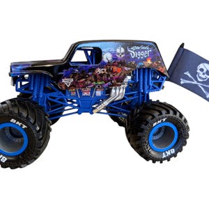 May include: A blue and black monster truck toy with large black tires and blue rims. The truck features a skull and crossbones flag and the words "Grave Digger" on the side.