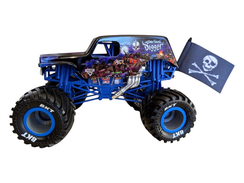 May include: A blue and black monster truck toy with large black tires and blue rims. The truck features a skull and crossbones flag and the words "Grave Digger" on the side.