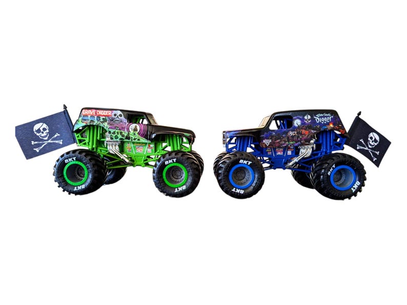 May include: Two toy monster trucks, one green and one blue, with large tires. The green truck has "Grave Digger" on the roof and a skull and crossbones flag. The blue truck has "Monster Jam" on the roof and a skull and crossbones flag.