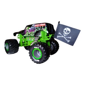 May include: A green and black Grave Digger monster truck toy with large black tires and green rims. The truck has a skull and crossbones flag and the words "Grave Digger" on the roof.