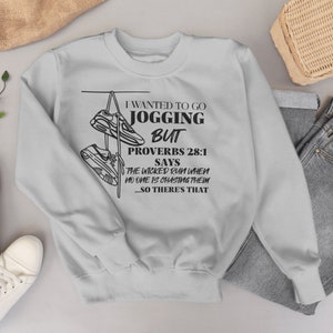 May include: Gray sweatshirt with a black graphic print of a pair of sneakers hanging from a line. The text reads "I wanted to go jogging but Proverbs 28:1 says the wicked run when no one is chasing them...so there's that."